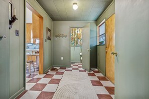A hallway with a checkered floor, a rug, and a window with floral curtains.