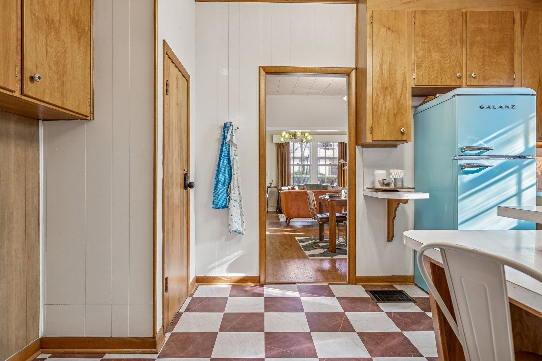 Une cuisine avec des meubles de rangement en bois, un réfrigérateur bleu et un sol à carreaux.