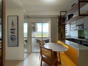 A modern kitchen with a dining area, large windows, and a view of the outdoors. - Solarium Beach Club -Apartamento T1.602 (Itapoá)