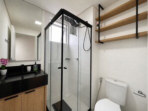 Uma casa de banho moderna com chuveiro em cabine de vidro, sanita e bancada preta com lavatório e espelho.
