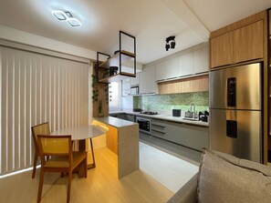A modern kitchen with a central island, built-in appliances, and a dining area with a table and chairs. - Solarium Beach Club -Apartamento T1.602 (Itapoá)