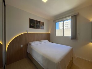A hotel room with a bed, a window with curtains, a wall-mounted artwork, and a bedside table. - Solarium Beach Club -Apartamento T1.602 (Itapoá)