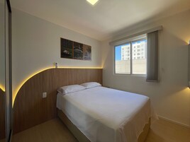 Quarto de hotel com cama, janela com cortinas, obra de arte na parede e mesa de cabeceira.