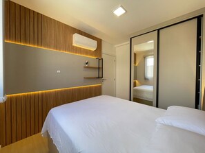 A modern bedroom with a bed, a wall-mounted air conditioner, and a sliding door closet. - Solarium Beach Club -Apartamento T1.602 (Itapoá)