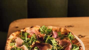 A pizza with greens and prosciutto on a white plate on a wooden table.