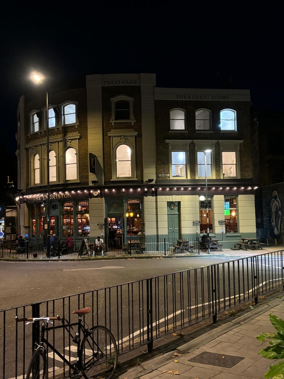 A building with 'FREEHOUSE PUB & GUEST ROOMS' signage, a street-level entrance with outdoor seating, and a bicycle parked outside.