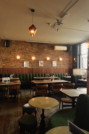 A restaurant interior with brick walls, green booths, wooden tables, and hanging pendant lights.