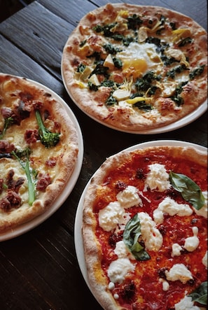 Tres pizzas sobre una mesa de madera.