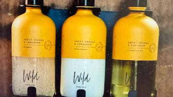 Three bottles of shampoo with pumps, labeled 'Sweet Orange & Cardamom,' and the brand 'Wild' visible on the bottles.