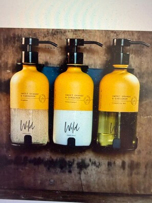 Tres botellas de champú con dispensadores, etiquetadas como 'Sweet Orange & Cardamom', y la marca 'Wild' visible en las botellas.