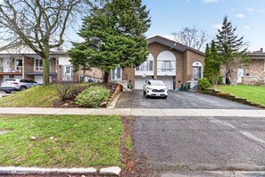 Een woonstraat met huizen, een witte auto geparkeerd voor een huis en een oprit naar een garage.