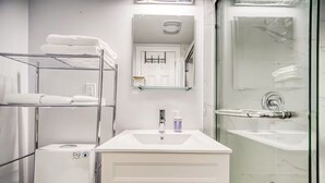 Um banheiro moderno com chuveiro de cabine de vidro, pia branca com dispensador de sabonete e porta-toalhas.