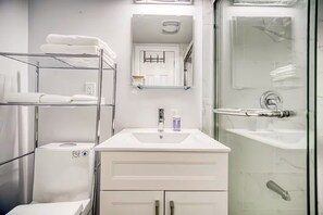 Een moderne badkamer met een douchecabine van glas, een witte wastafel met zeepdispenser en een handdoekrek.