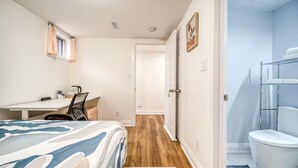 Quarto com cama, escrivaninha, cadeira e banheiro com vaso sanitário e chuveiro.