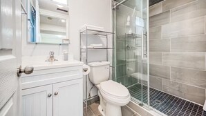 Um banheiro moderno com vaso sanitário, box de vidro e toucador branco com espelho.