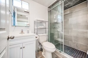 Een moderne badkamer met toilet, een douchecabine van glas en een wit wastafelmeubel met spiegel.