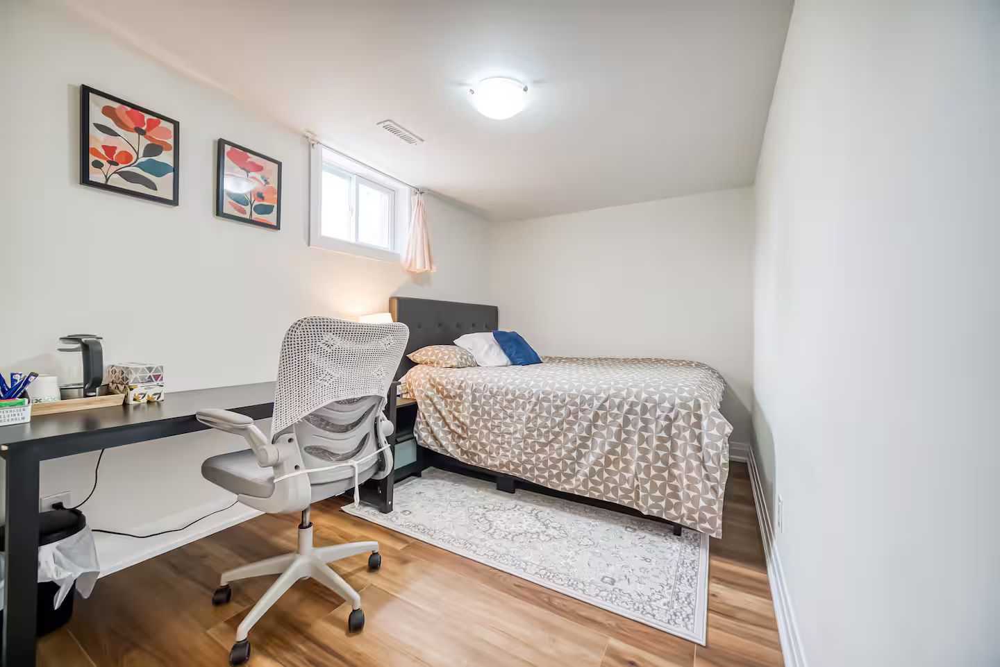 Ein Schlafzimmer mit einem Bett, einem Schreibtisch mit Stuhl, einem Fenster und zwei Bildern an der Wand.