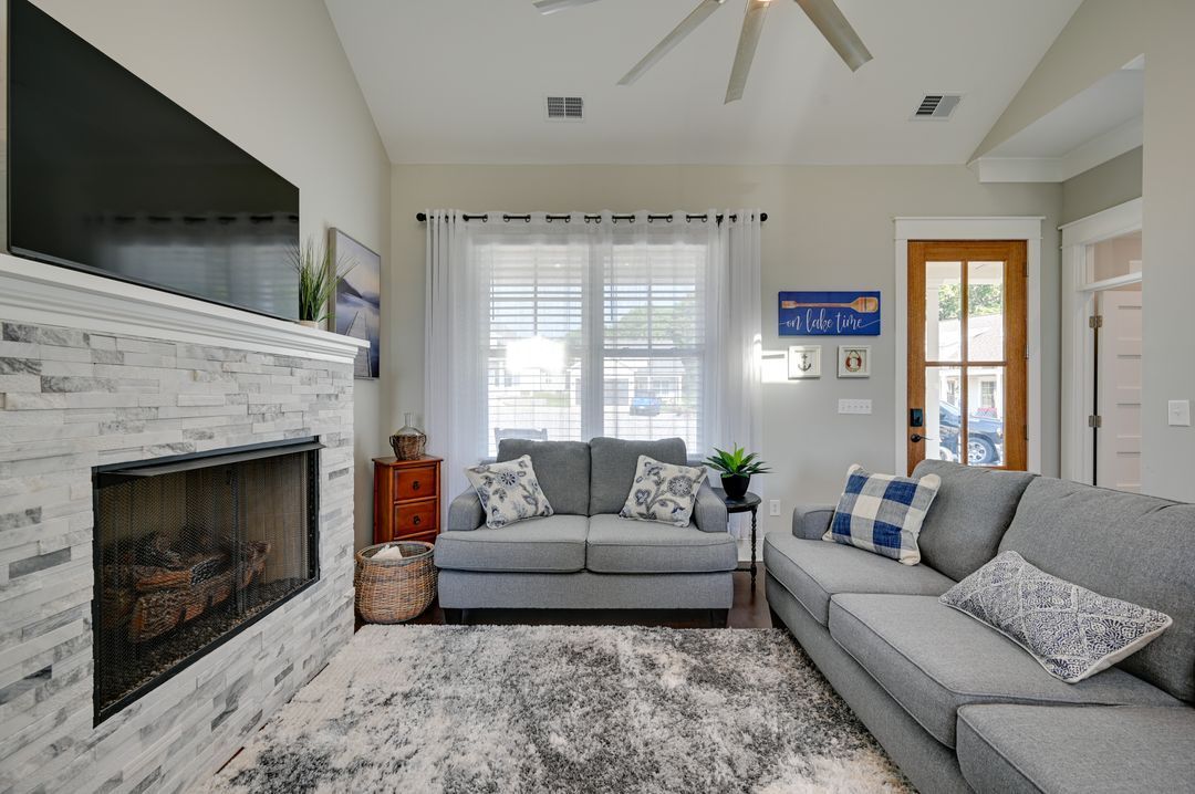 A living room with a fireplace, a grey sofa, a blue sign, and a ceiling fan.