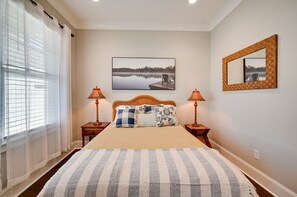 A bedroom with a large bed, two bedside tables with lamps, a framed picture on the wall, and a window with curtains. - Relax by Lake Greenwood | Porch, Grill & More (Greenwood)