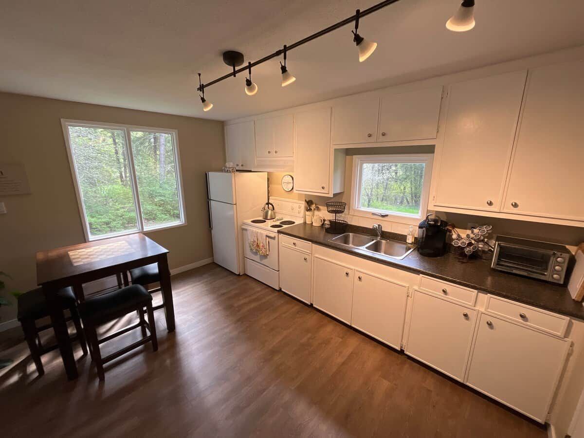 A kitchen with white cabinets, a stove, a sink, and a dining table with chairs.
