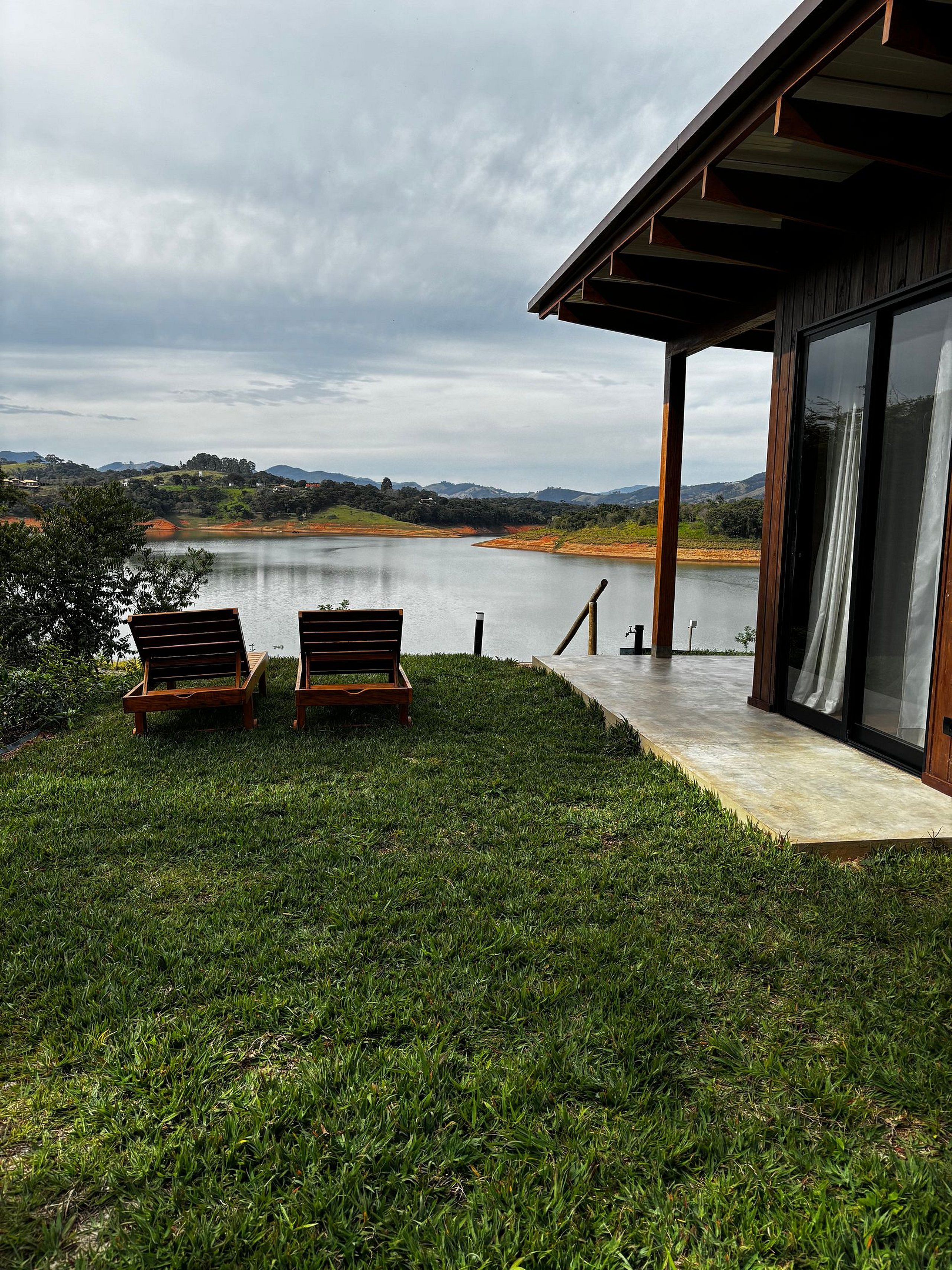 A modern building with a glass door leading to a deck overlooking a lake.