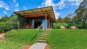 Un edificio moderno con entrada cubierta, escalones de madera que lo conducen y un banco en el jardín.