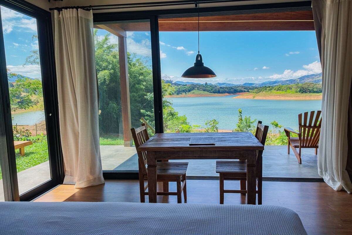 Ein Zimmer mit einer großen Schiebeglastür, die Blick auf einen See gewährt, einem Holztisch mit Stühlen und einer hängenden Pendelleuchte.