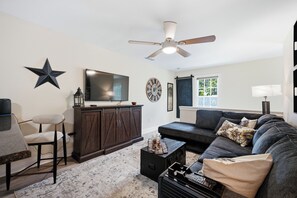 Una sala de estar con un mueble de madera oscura, un televisor, una decoración con forma de estrella, un reloj y un ventilador de techo.