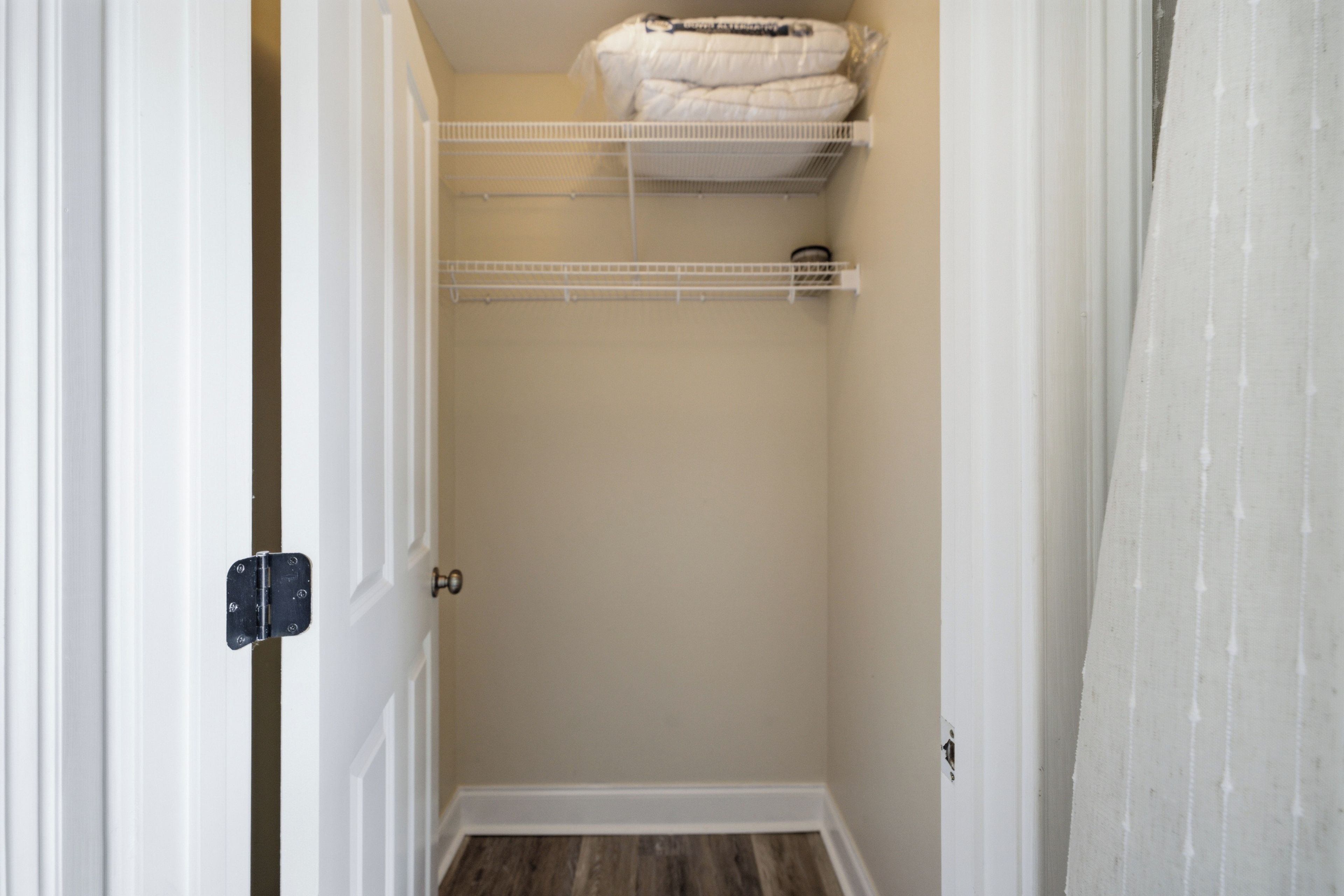 A walk-in closet with a white door, a metal shelf unit, and a wooden floor.