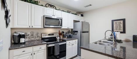 A modern kitchen with white cabinets, a stainless steel microwave, a refrigerator, and a coffee maker.