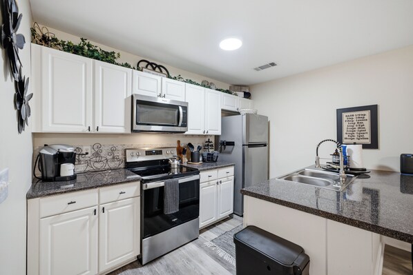 Una cocina moderna con armarios blancos, un microondas de acero inoxidable, un refrigerador y una cafetera.