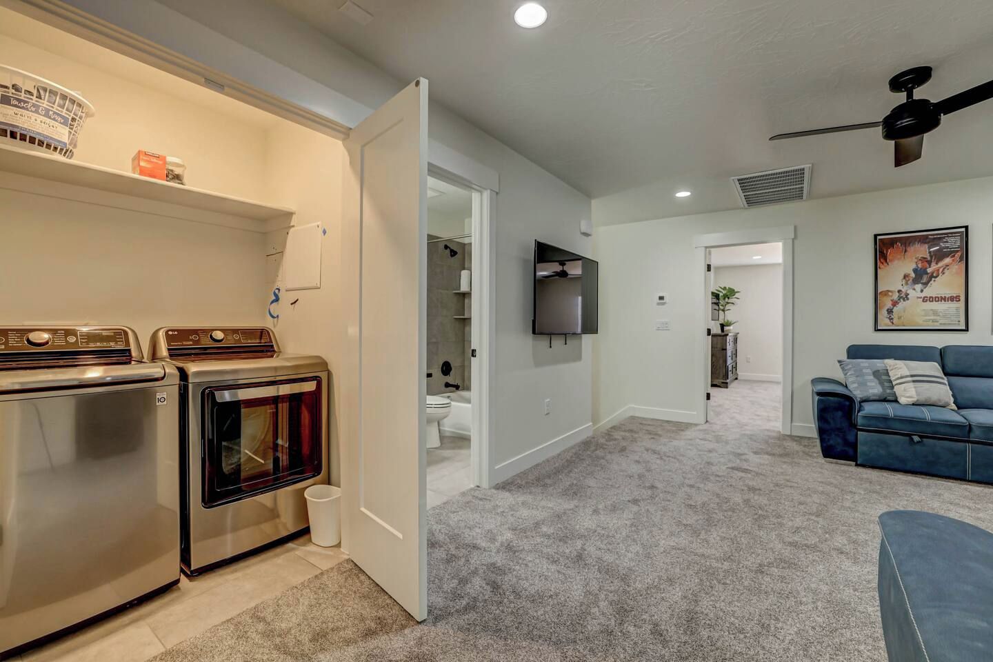 Un espacio habitable compacto con kitchenette, un sofá azul y un televisor fijado a la pared.