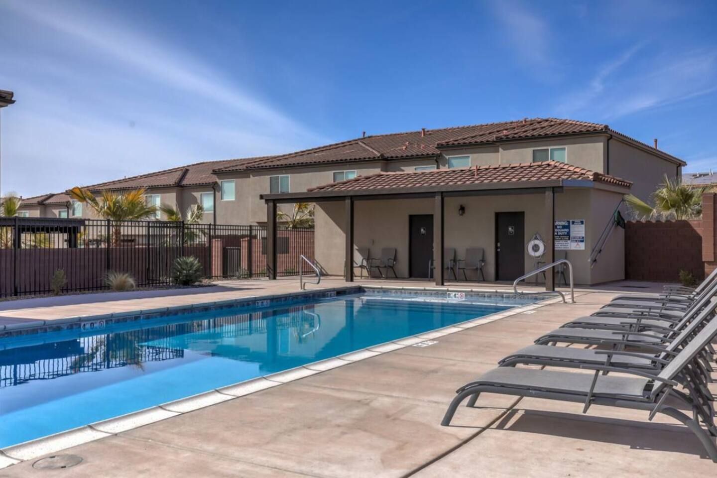 A swimming pool with lounge chairs, a covered area, and a building with a tiled roof.