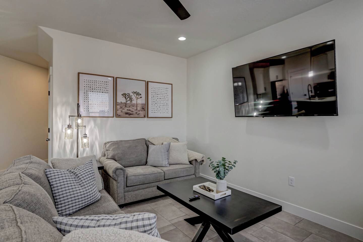 A living room with a grey sofa, a coffee table, and a flat-screen TV mounted on the wall.