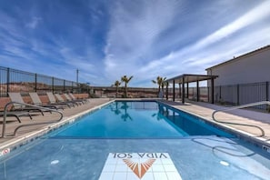 A swimming pool with lounge chairs and a covered area, surrounded by a fence and palm trees. - Private Hot Tub, Fire Pit, BBQ, Heated Pool Near Zion & Sand Hollow (Washington)
