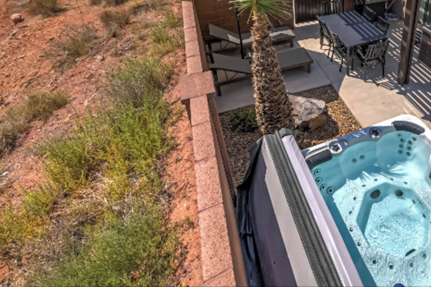 A hot tub with a stone border, a palm tree, and outdoor furniture.
