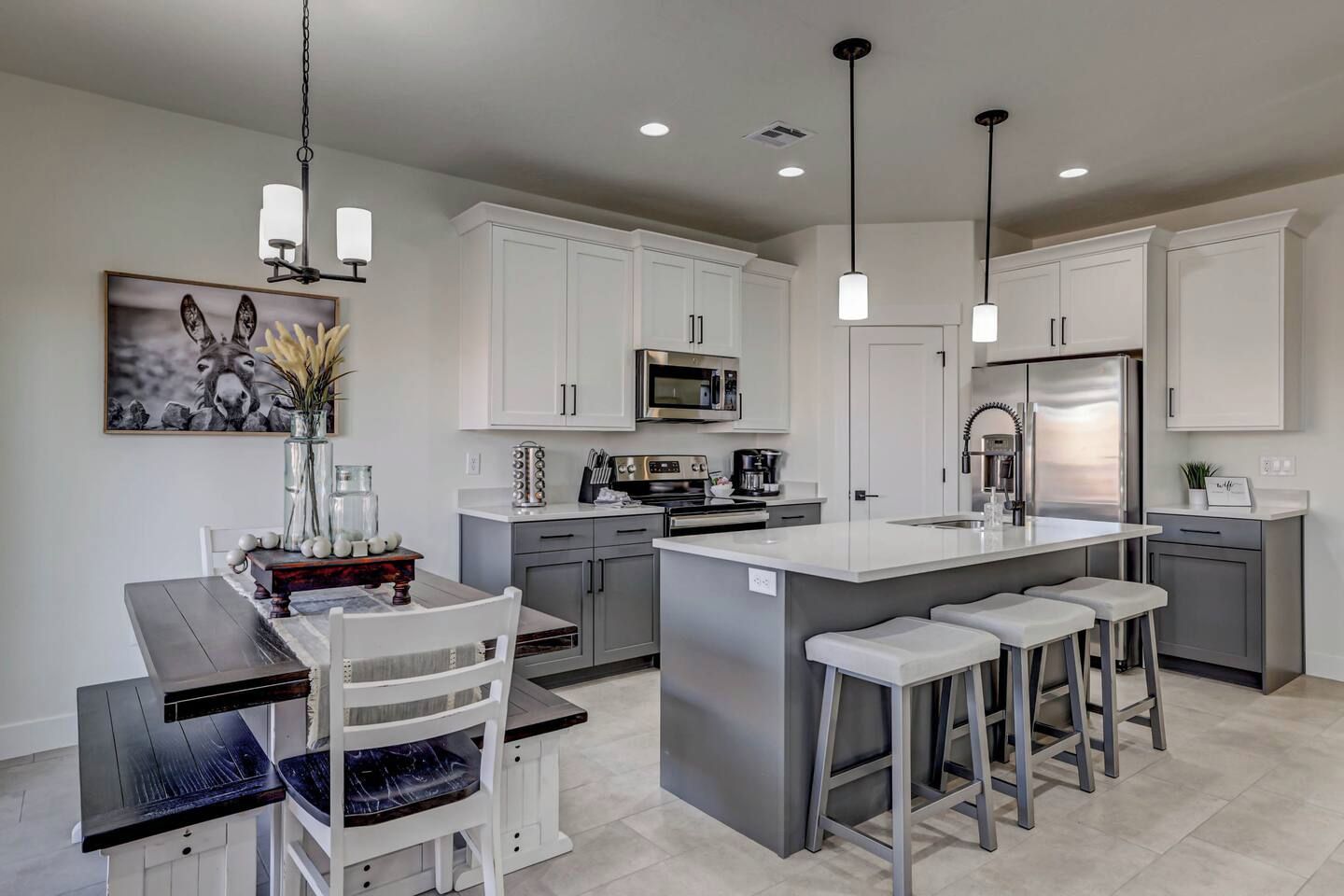 Eine moderne Küche mit weißen Schränken, Edelstahlgeräten, einer zentralen Kochinsel inklusive Barhocker und Pendelleuchten.