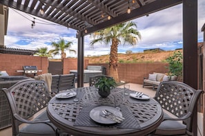 An outdoor patio with a round table set for dining, surrounded by wicker chairs, a grill, and a hot tub. - Private Hot Tub, Fire Pit, BBQ, Heated Pool Near Zion & Sand Hollow (Washington)