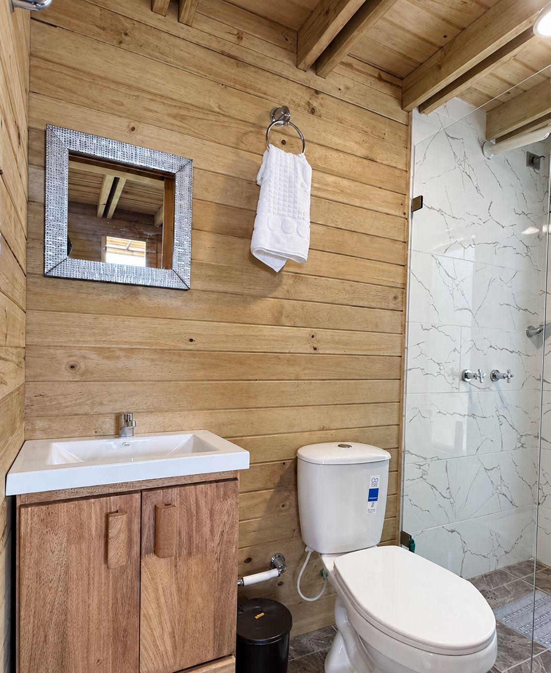 A wooden bathroom with a sink, toilet, and a glass shower enclosure.