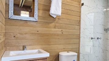 A wooden bathroom with a sink, toilet, and a glass shower enclosure.