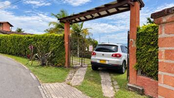 Un camino de entrada cerrado con portón que conduce a un auto blanco estacionado bajo una pérgola.