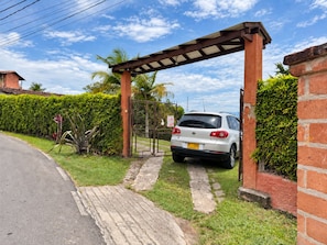 Un camino de entrada cerrado con portón que conduce a un auto blanco estacionado bajo una pérgola.