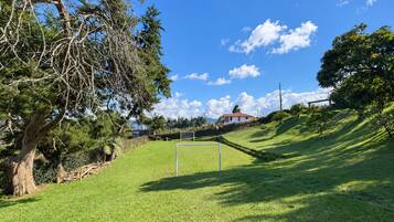 Un campo cubierto de césped con un arco, árboles y una casa al fondo.
