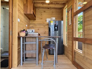 A compact kitchen with a stainless steel refrigerator, a sink, and a small dining area with stools.