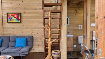 Un intérieur en bois comprenant un canapé, une sculpture décorative en bois, et une salle de bain visible à travers une porte ouverte.