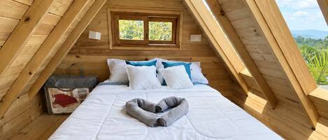 A bedroom with a wooden ceiling, a bed with white bedding, and a window with a view of greenery.