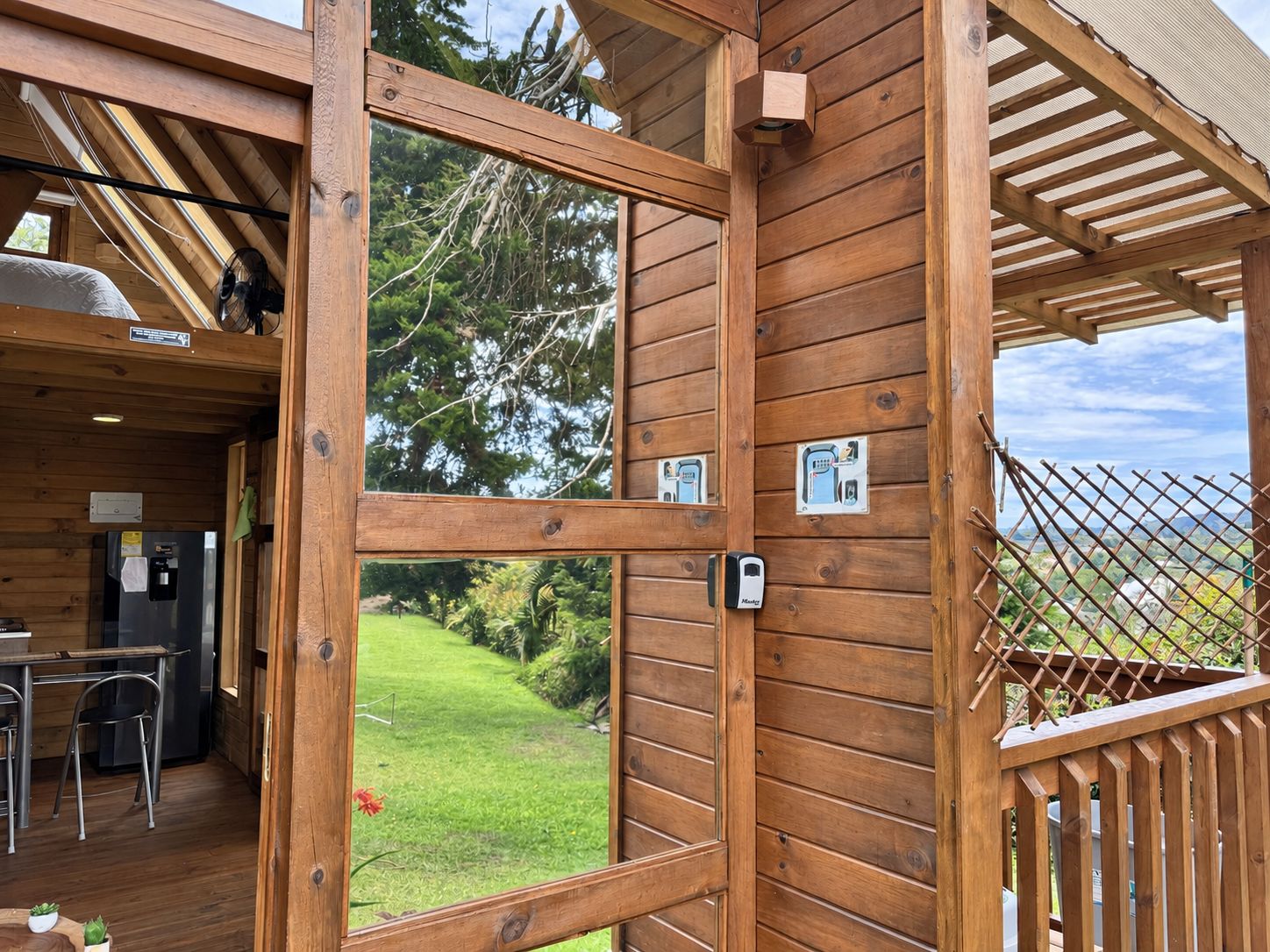 Une cabane en bois dotée d’une grande fenêtre, d’un coin cuisine et offrant une vue sur un paysage verdoyant.