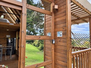 A wooden cabin with a large window, a kitchen area, and a view of a green landscape.