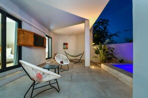 A modern outdoor patio with two white wicker chairs, a small table, and a pool with blue lighting. - Casa Romelli • Luxury 5BR Family Villa • Pool, Whirlpool & Tropical Garden by Bocobay (Noord)