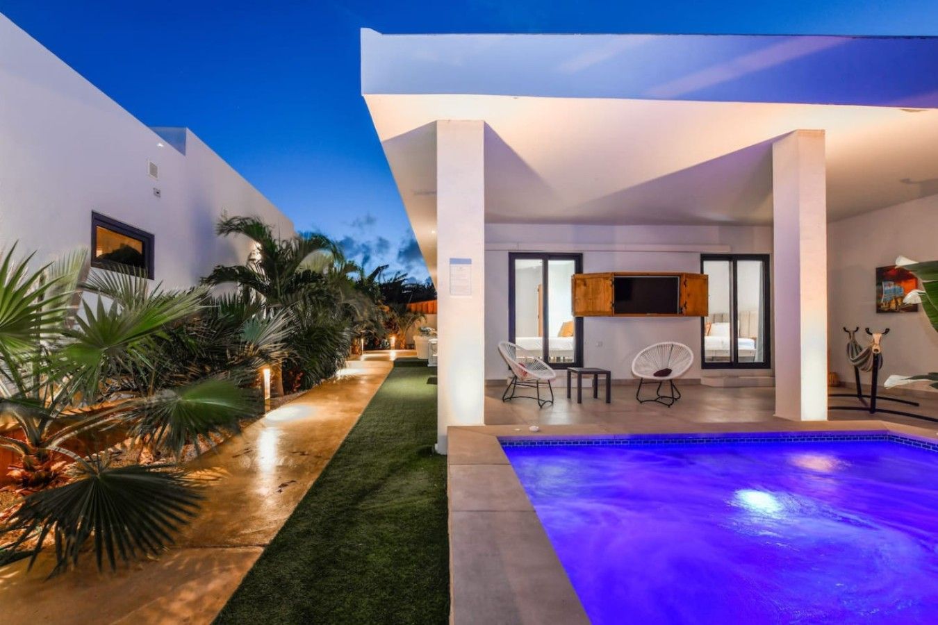 A modern outdoor pool area with a clear sky, a well-maintained lawn, and a seating area with two chairs.